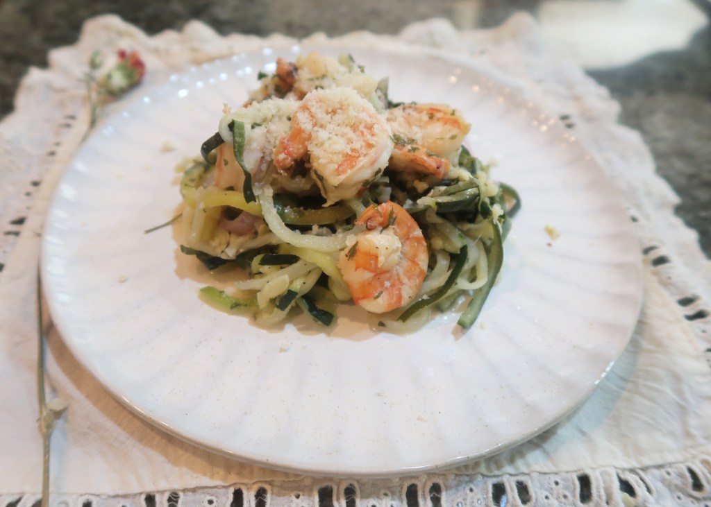 A plate of zucchini noodles topped with shrimp and sprinkled with grated cheese, placed on a decorative linen napkin.
