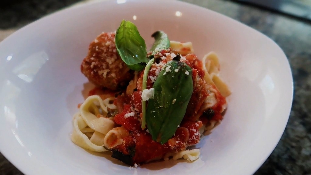 A bowl of spaghetti topped with turkey meatballs, tomato sauce, fresh basil, and grated cheese.
