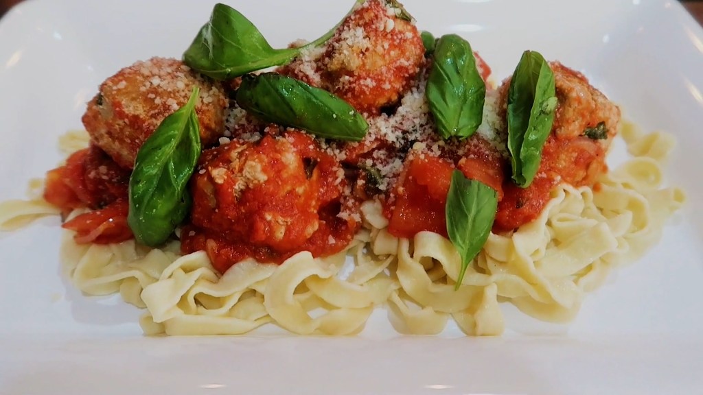 A plate of freshly made fettuccine topped with turkey meatballs, marinara sauce, and garnished with basil leaves and grated cheese.