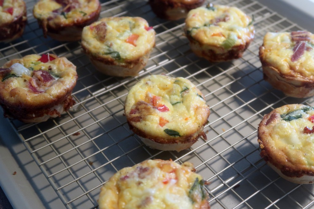 Baked egg muffins with colorful vegetables displayed on a cooling rack.